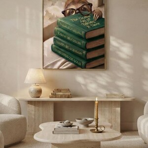 Wide view of a neutral living room with the sloth peeking over books print framed above a low sofa in soft daylight