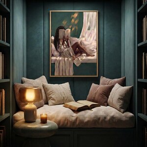 Gold-framed emerald green art print of a Black woman reading on a window seat on a deep green panelled wall above a built-in reading nook, with a lamp, candles, an open book and layered cushions.