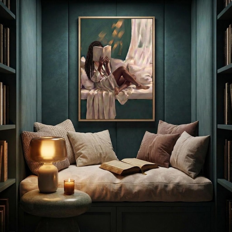 Gold-framed emerald green art print of a Black woman reading on a window seat on a deep green panelled wall above a built-in reading nook, with a lamp, candles, an open book and layered cushions.