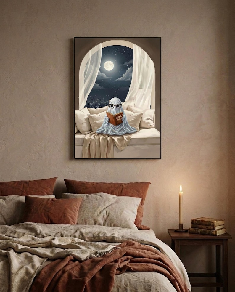 Painterly print of a small ghost in round glasses reading in bed by a moonlit window, holding a book titled Ghostly Tales, framed above a bed with linen bedding and a lit candle on the nightstand