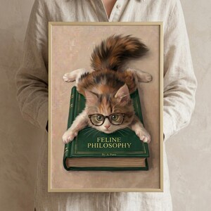 A person in a linen shirt holding the calico kitten wall art print in a slim gold frame against a soft neutral background