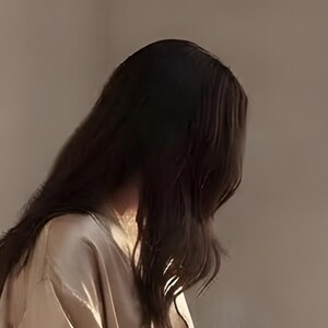 Close-up detail from Reading Nook Decor, a cropped fragment of the printable artwork: long dark hair falling in loose waves over a satin robe, lit by warm light against a plaster wall.