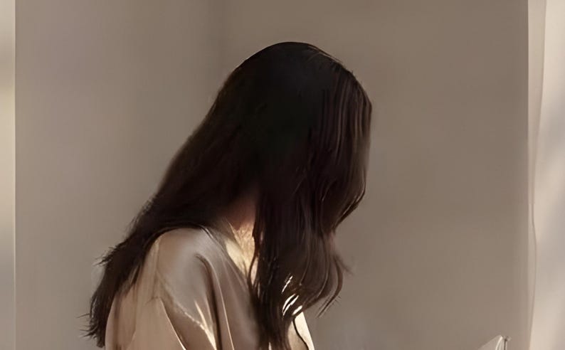 Close-up detail from Reading Nook Decor, a cropped fragment of the printable artwork: long dark hair falling in loose waves over a satin robe, lit by warm light against a plaster wall.