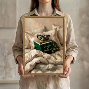 Person in a linen shirt holding the framed tortoise reading print in a slim gold frame, showing its true scale against a soft neutral background