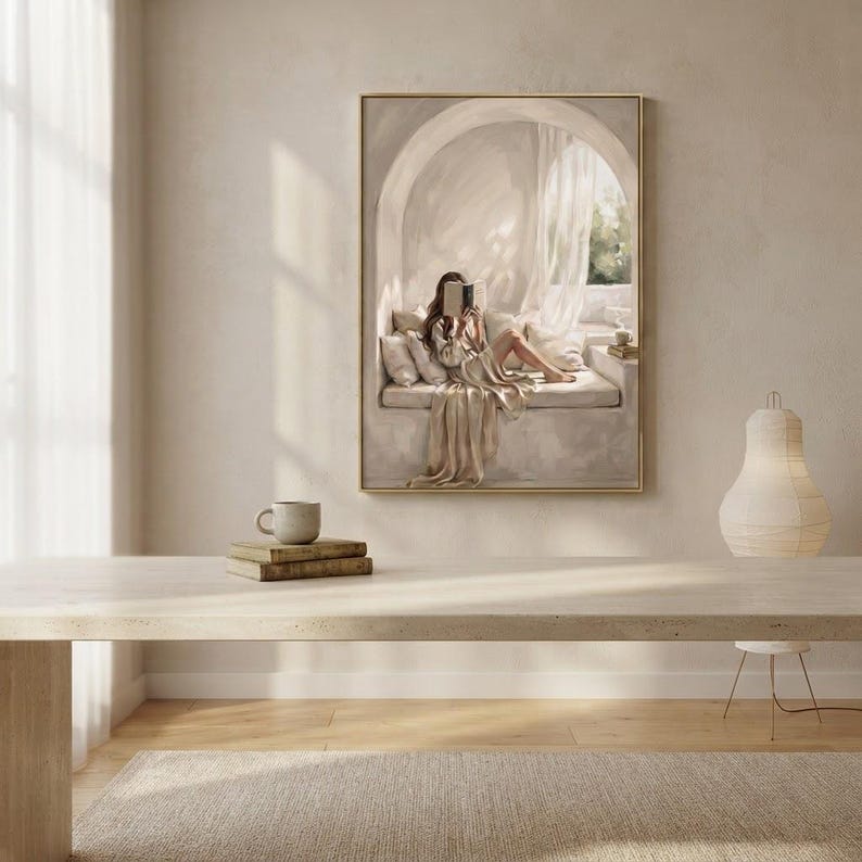 Woman reading nook wall art hung in a quiet bedroom with textured plaster walls, linen bedding, and a thin gold frame, no mat.