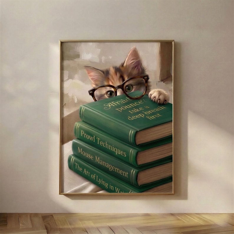 Framed print of a tabby kitten in tortoiseshell glasses peeking over four green clothbound books lettered in gold, hanging on a bare warm plaster wall above a pale oak herringbone floor in soft daylight.