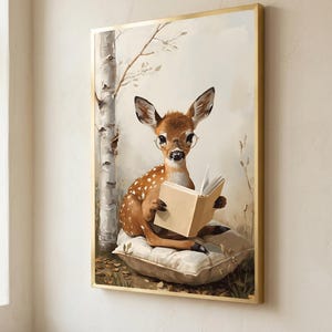 Framed woodland nursery print of a fawn in round glasses reading a book, hanging on a soft white plaster wall in a slim gold frame