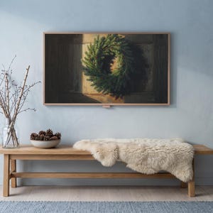 Wreath on a dark door art from the set on a Frame TV in a cool winter room with a pale blue wall, an oak bench with sheepskin, birch branches and snow outside