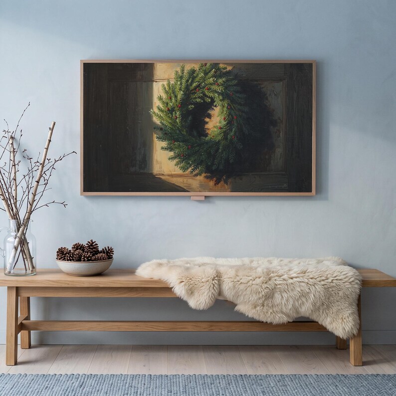Wreath on a dark door art from the set on a Frame TV in a cool winter room with a pale blue wall, an oak bench with sheepskin, birch branches and snow outside