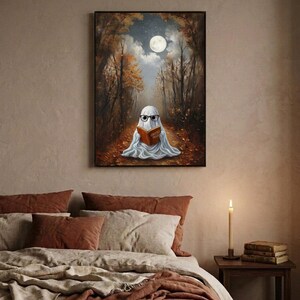 The autumn forest ghost reading print framed above a bed with linen bedding and a lit candle on the nightstand