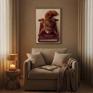 Framed squirrel on a book print above a linen armchair in a warm reading corner, with an open book and reading glasses on the seat and a lit lamp on a side table