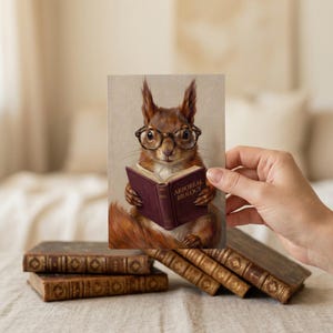 A hand holding a small four by six inch squirrel reading print above a stack of antique leather books