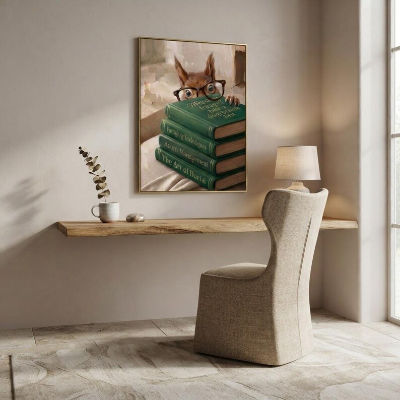Squirrel in round glasses peeking over books print framed above a restrained workspace with pale walls and a natural linen chair