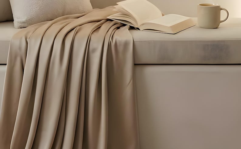 Close-up detail from Reading Nook Quiet Corner, a cropped fragment of the printable artwork: a linen throw draped over a window seat with an open book and a ceramic mug.