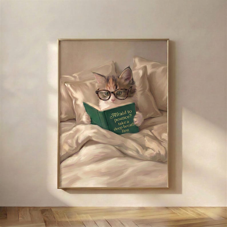 Painterly print of a calico kitten in round tortoiseshell glasses propped on linen pillows, reading a green clothbound book lettered in gold hung on a wall as wall art.