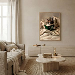 The framed cat reading print hanging above a cream sofa in a calm, light-filled living room