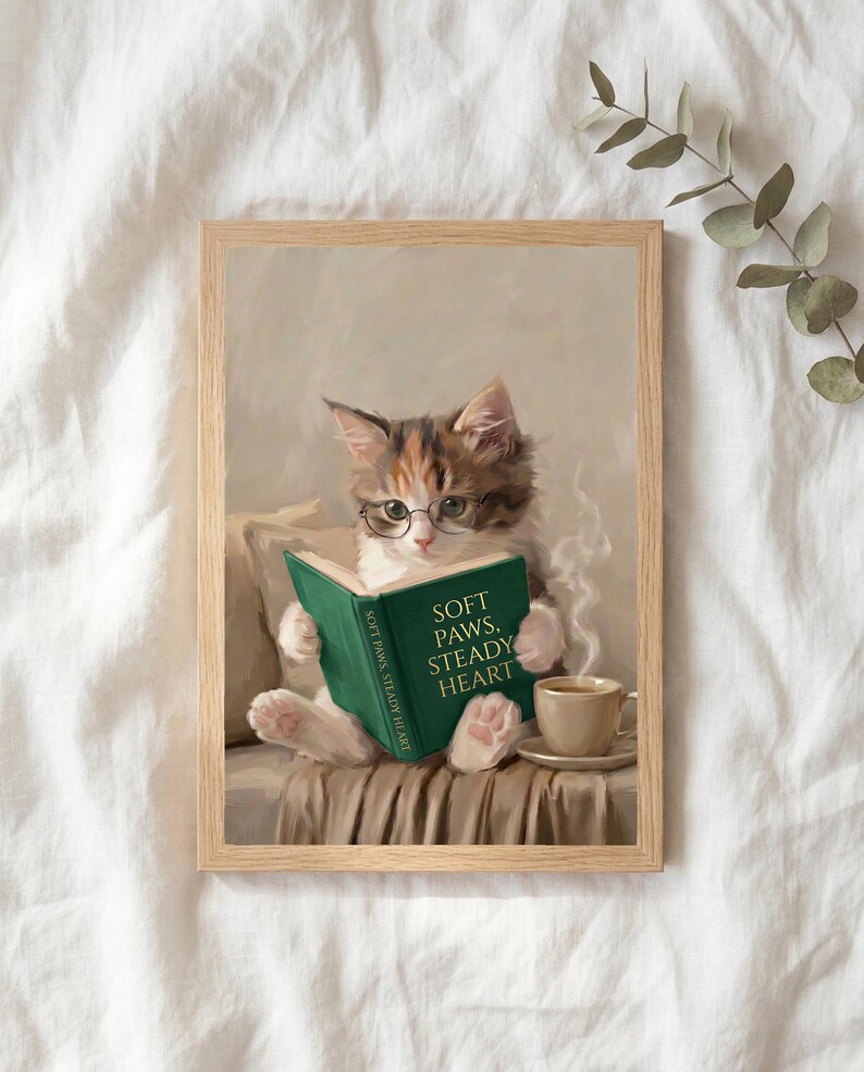 The kitten reading print in a thin natural oak frame lying on white linen with a sprig of eucalyptus