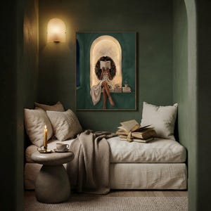 Emerald green reading nook art print above a cream linen daybed in a dark green reading alcove, with a wall sconce, a lit candle, a cup of tea and a stack of antique books.