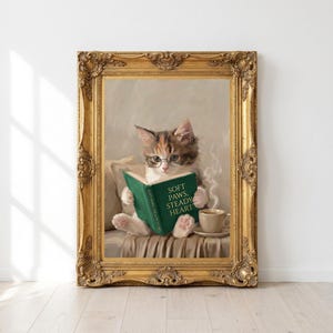 Printable kitten reading print in an ornate antique gold frame leaning against a white wall on a pale oak floor in morning sunlight