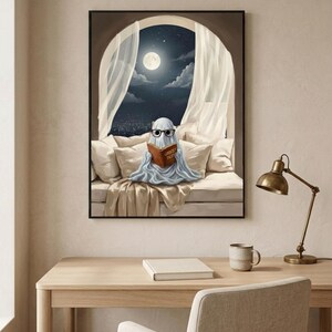 The moonlit bed ghost reading print framed above a pale oak desk with a stoneware mug and a brass lamp