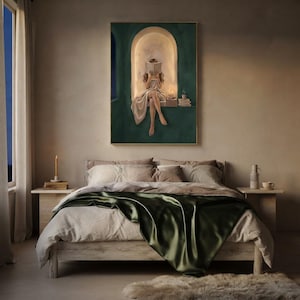 Emerald green reading nook art print above a rustic wooden bed dressed in linen and deep green silk, on a plaster bedroom wall with a candle, a stoneware jug and a night window.