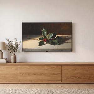 May include: A rectangular wall-mounted television displaying a still life painting of a sprig of green holly leaves with bright red berries resting on a light-colored surface against a dark brown background, positioned above a long wooden media console.