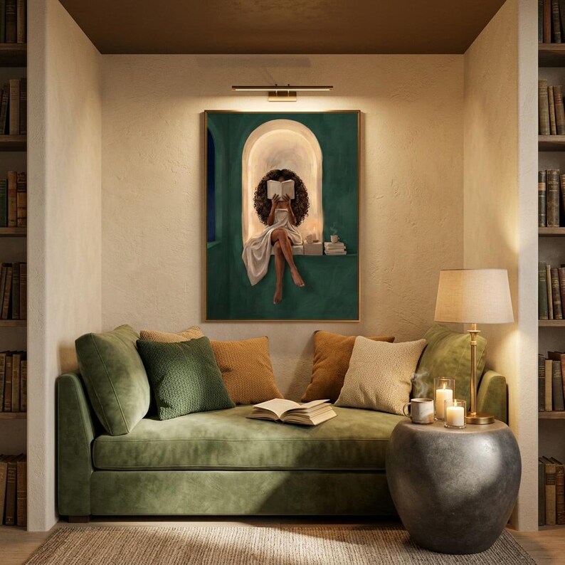 Emerald green reading nook art print hung above a green velvet daybed in a cosy library alcove, lit by a brass picture light, with bookshelves either side and candles on a stone side table.