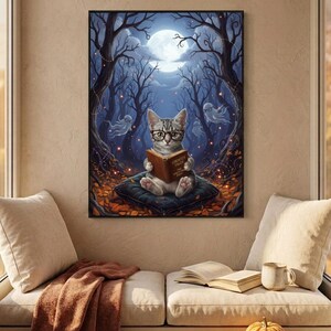 The kitten and ghosts ghost reading print framed above a cushioned window bench with a wool throw and a small pumpkin