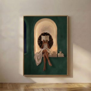 Emerald green reading nook art print of a Black woman with voluminous curls reading by candlelight, in a thin gold frame on a plain plaster wall.