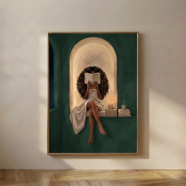 Emerald green reading nook art print of a Black woman with voluminous curls reading by candlelight, in a thin gold frame on a plain plaster wall.