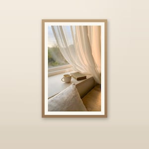 Japandi window seat wall art print with wooden frame, book and coffee on sunlit ledge, sheer beige curtains, minimalist Scandinavian home decor, slow living interior, neutral calming room accent, digital printable art