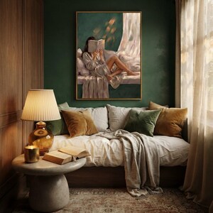 Emerald green wall art framed in gold, hanging above a linen daybed in a wood-paneled reading corner with olive and mustard velvet pillows, a lit candle and lamp on a round stone table.