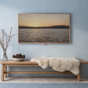 Winter dusk in blue art from the set on a Frame TV in a cool winter room with a pale blue wall, an oak bench with sheepskin, birch branches and snow outside
