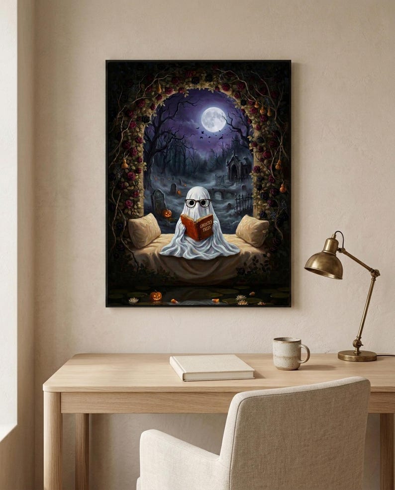 The graveyard arch ghost reading print framed above a pale oak desk with a stoneware mug and a brass lamp