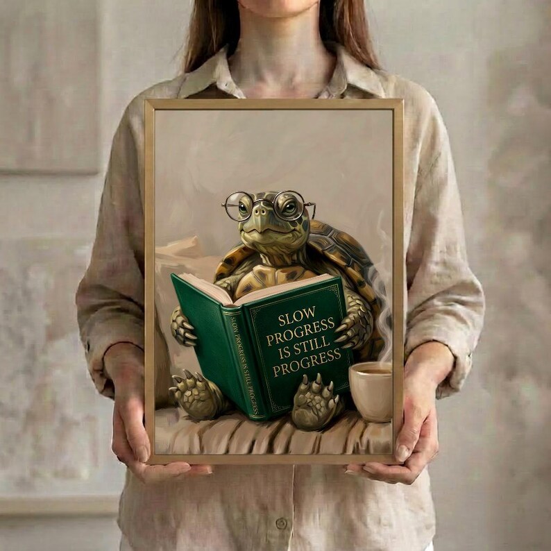 A person in a linen shirt holding the tortoise reading art print in a slim gold frame against a soft neutral background