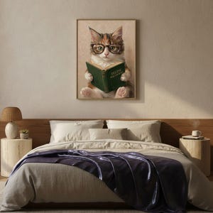 Painterly print of a calico kitten in round tortoiseshell glasses reading a green book framed on a textured plaster bedroom wall above linen bedding in soft morning light