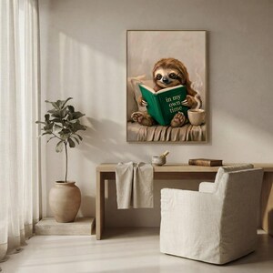 Sloth in glasses reading print framed above a restrained workspace with pale walls and a natural linen chair