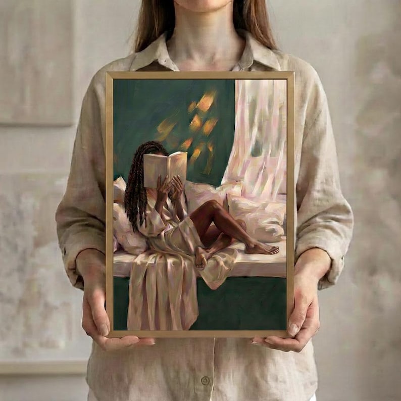 The emerald green art print of a Black woman reading on a window seat in a thin gold frame, held up in both hands to show its size.