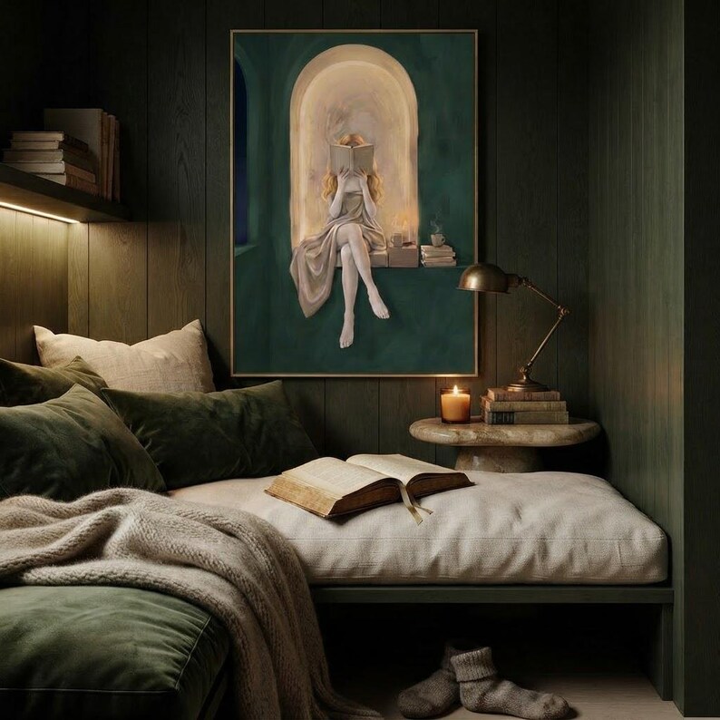 Emerald green reading nook art print in a dark green panelled reading nook, above a cushioned daybed with velvet pillows, a knit throw, a brass desk lamp and an open book.