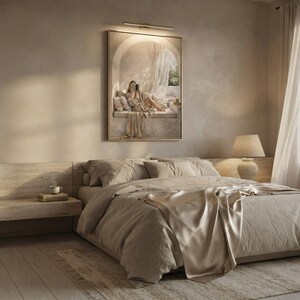 Woman reading nook wall art hung in a quiet bedroom with textured plaster walls, linen bedding, and a thin gold frame, no mat.