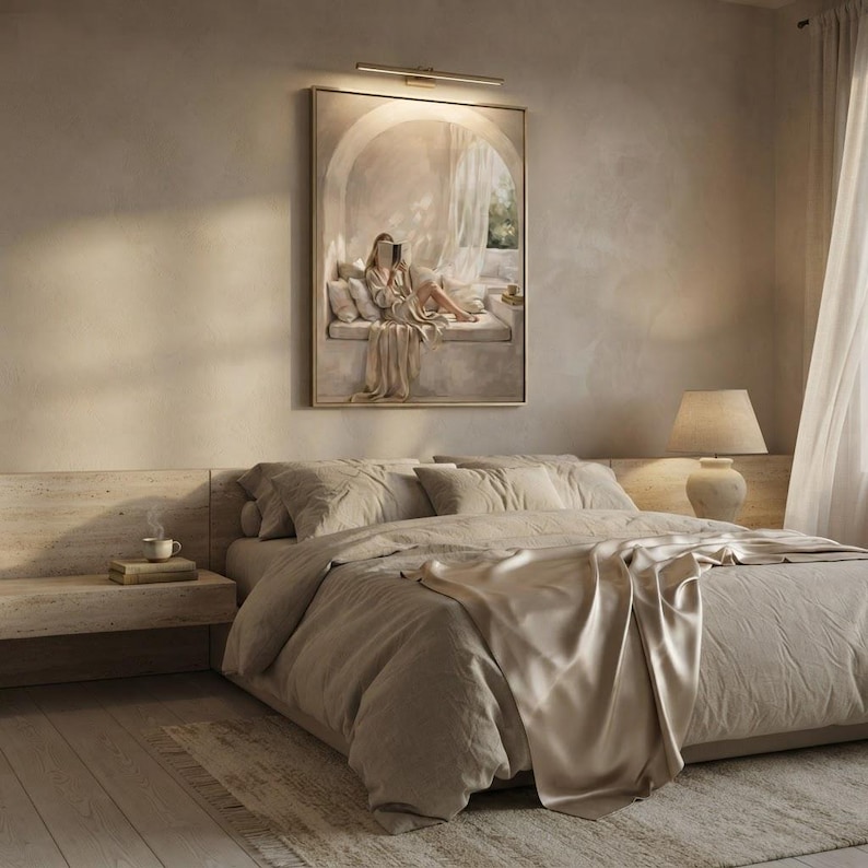 Woman reading nook wall art hung in a quiet bedroom with textured plaster walls, linen bedding, and a thin gold frame, no mat.