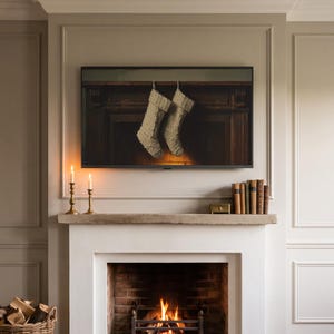 May include: A flat-screen television mounted above a fireplace displays an image of two cream-colored cable-knit stockings hanging from a dark wooden mantelpiece. The fireplace below contains a burning fire with visible orange flames and logs.