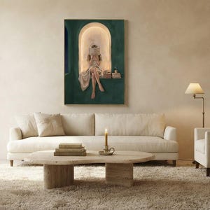 Emerald green reading nook art print above a long cream sofa in a bright plaster living room, with a travertine coffee table, a brass floor lamp, a lit candle and a deep wool rug.
