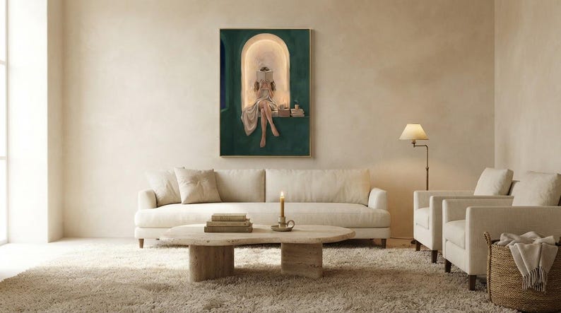 Emerald green reading nook art print above a long cream sofa in a bright plaster living room, with a travertine coffee table, a brass floor lamp, a lit candle and a deep wool rug.