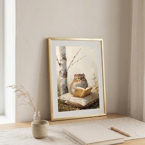 Framed print of a chipmunk in round glasses reading a book, leaning on a wooden desk beside a small vase and notebook in soft daylight
