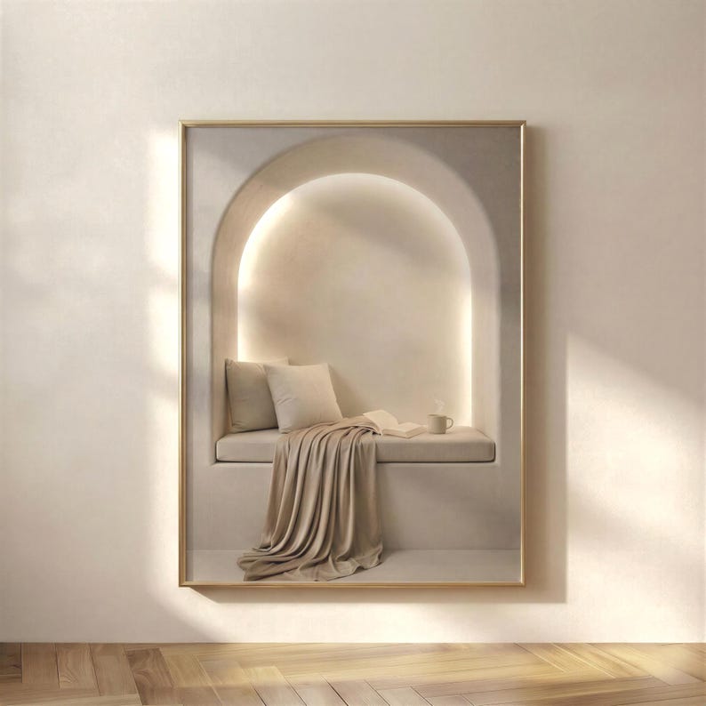 Neutral reading nook wall art in a thin gold frame hung on a warm beige wall above light herringbone flooring, soft plaster arch with cushions and draped linen, no mat.