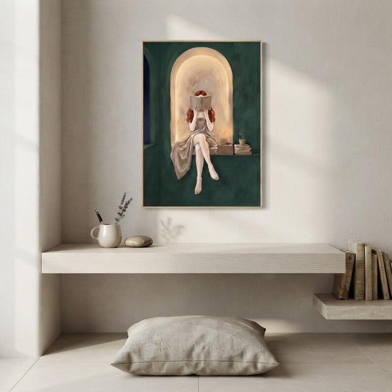 Emerald green reading nook art print on a pale plaster wall above a floating oak ledge with a stoneware jug of lavender, a floor cushion below and old books stacked to one side.