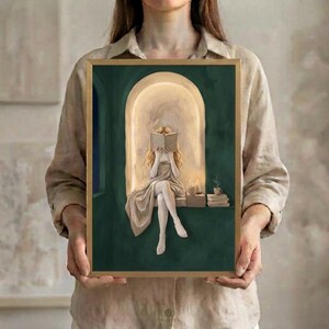 The blonde woman reading in an emerald green arched nook art print in a thin gold frame, held up in both hands to show its size.