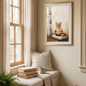 Framed print of a red fox reading a book, hung above a linen window seat with a stack of books, a mug and a fern in a bright neutral reading nook