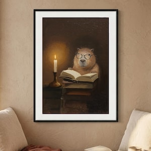 Framed print of a capybara in round wire-rimmed glasses reading by candlelight, hung above a cushioned window seat with an open book and a stoneware mug on the linen cushions.